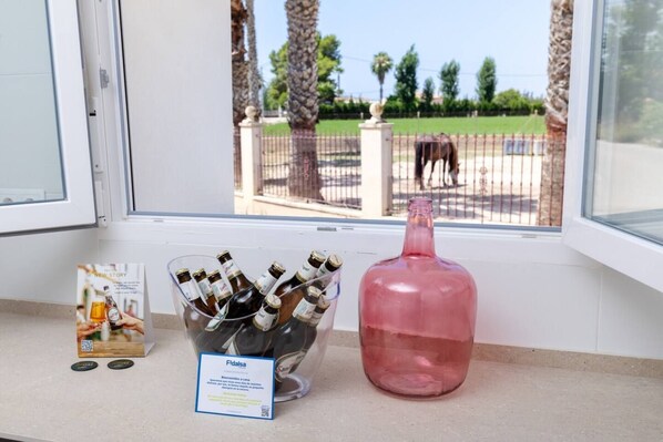 A window with a view of a fenced area, a bottle of pink liquid, and a container of beer bottles.
