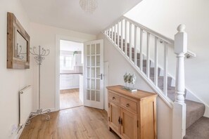 A hallway with a wooden floor, a white radiator, a white door, a wooden cabinet, and a staircase with white railings.