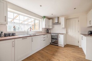 A kitchen with white cabinets, a stainless steel stove, a window with a view, and a wooden floor. - 3-Bed Home- Parking & Large Garden By Tempstay (Windsor)