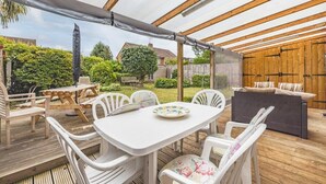 Een terras buiten met een tafel en stoelen, een bank en een pergola.