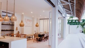 A modern kitchen with a central island, wooden chairs, and hanging pendant lights. - The Hut Hut (Pecatu)