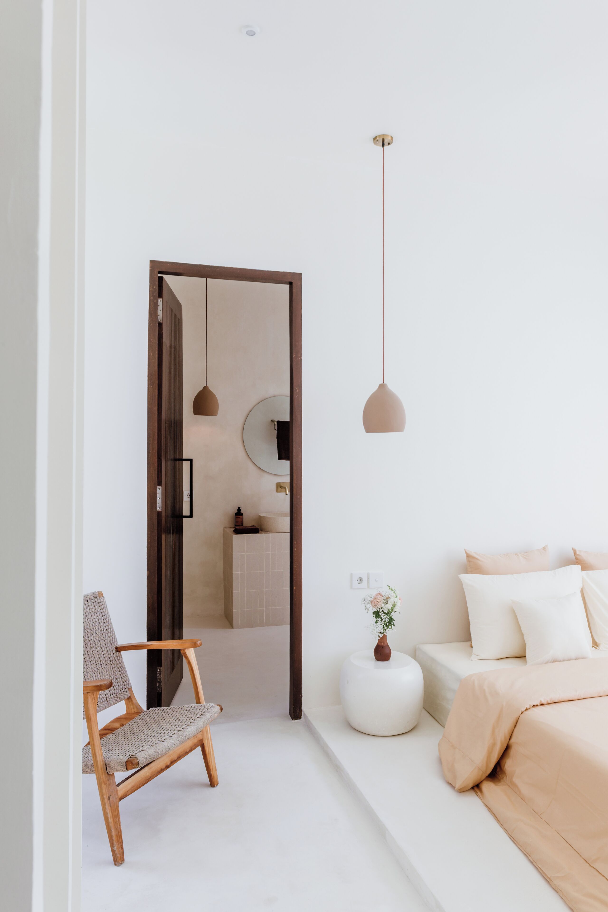 A modern bedroom with a bed, a chair, a bedside table, and a hanging light fixture.