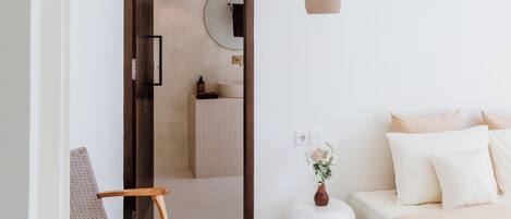 A modern bedroom with a bed, a chair, a bedside table, and a hanging light fixture.