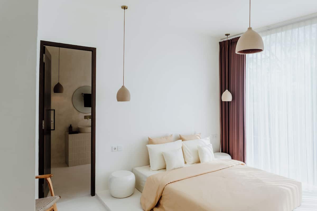 A modern bedroom with a bed, bedside tables, a mirror, and a window with curtains.