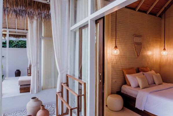 A bedroom with a bed, bedside lamps, and a view of the outdoors. - The Hut Hut (Pecatu)