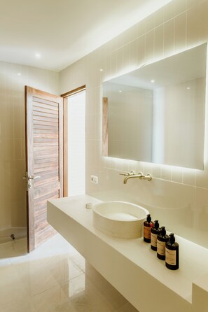 A modern bathroom with a large mirror, a round sink, and a wooden door. - The Hut Hut (Pecatu)