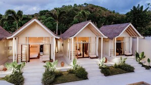 A resort with three bungalow-style accommodations, each with a thatched roof and large windows. - The Hut Hut (Pecatu)