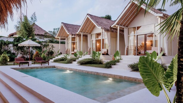 A poolside area with a pool, lounge chairs, and a thatched-roof building. - The Hut Hut (Pecatu)