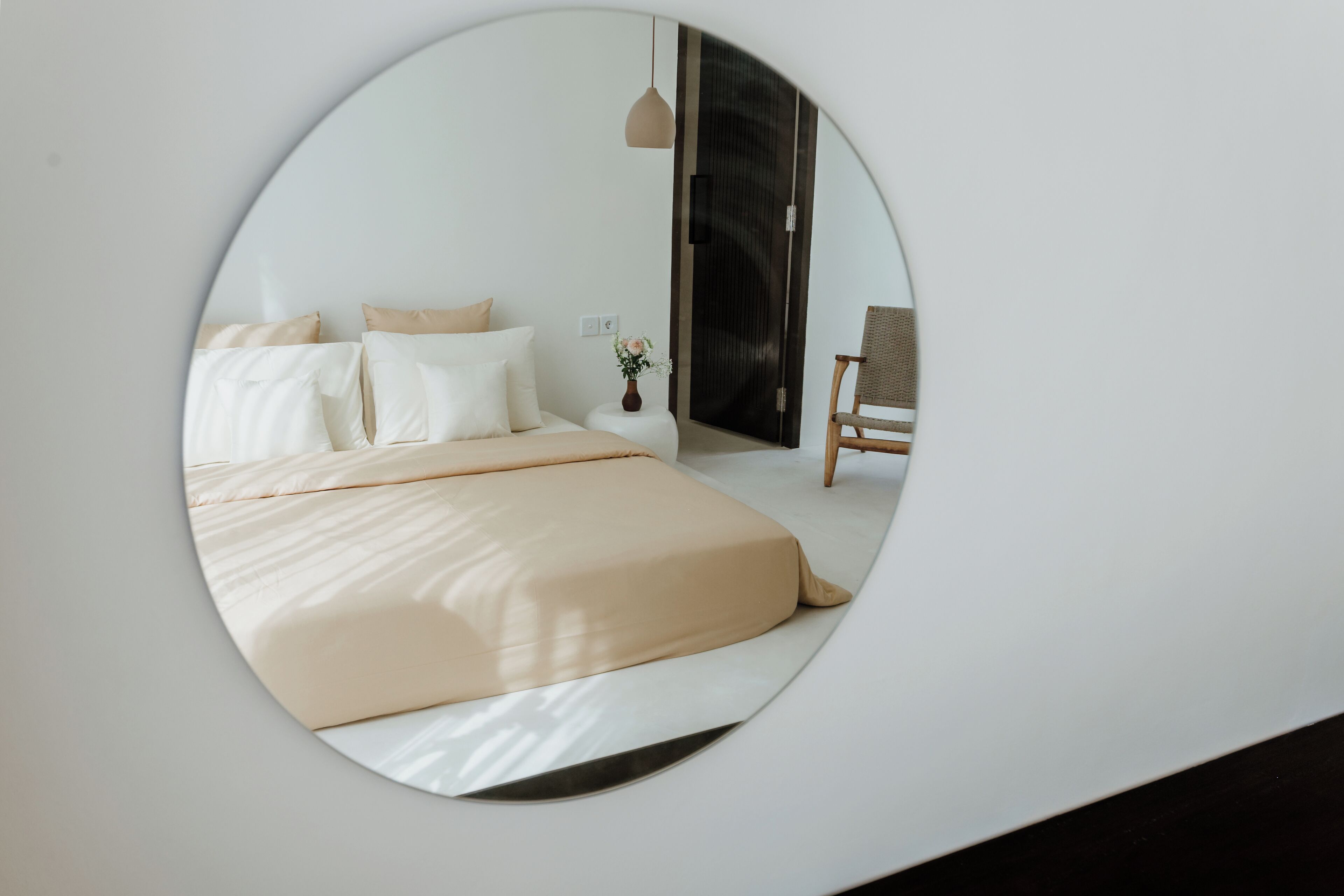A bedroom with a bed, pillows, a nightstand, a vase with flowers, a chair, and a wardrobe.