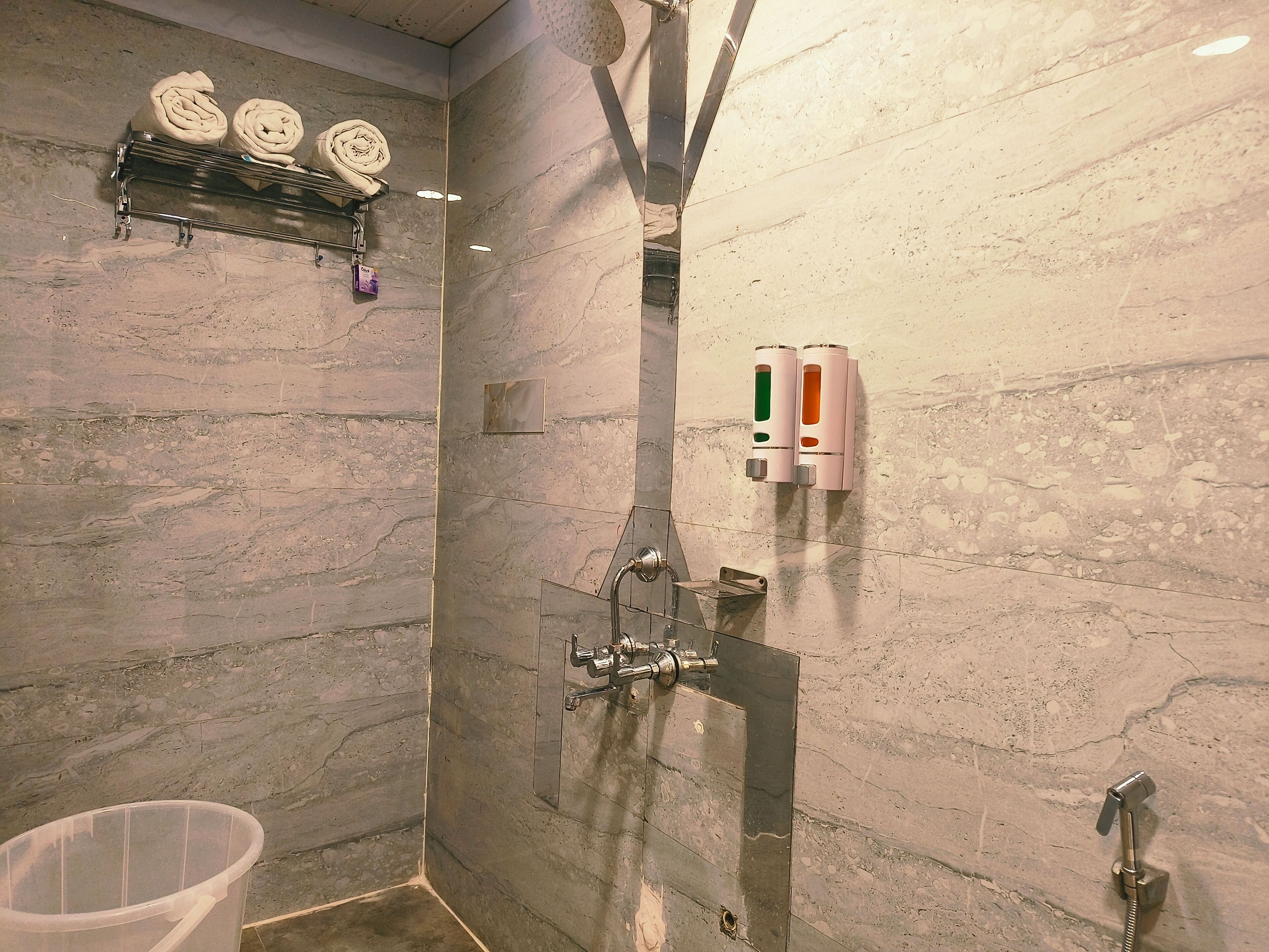 A bathroom with a shower, a towel rack, and a soap dispenser.