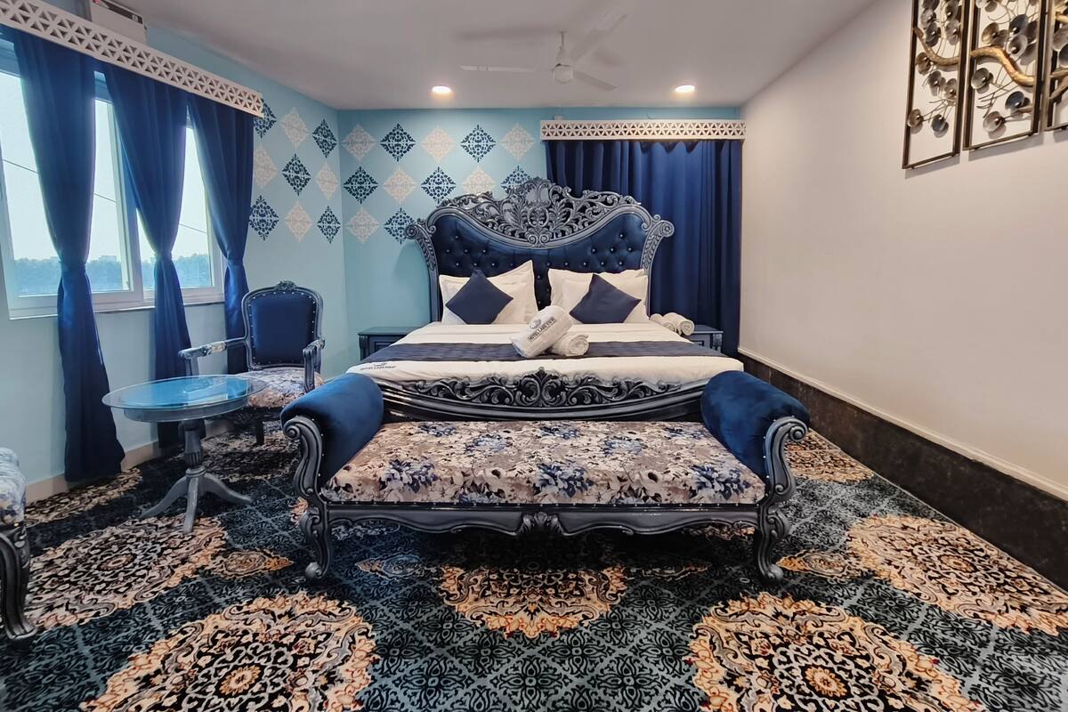 Een slaapkamer met een groot bed, een stoel, een klein tafeltje en een kamer met een patroon.