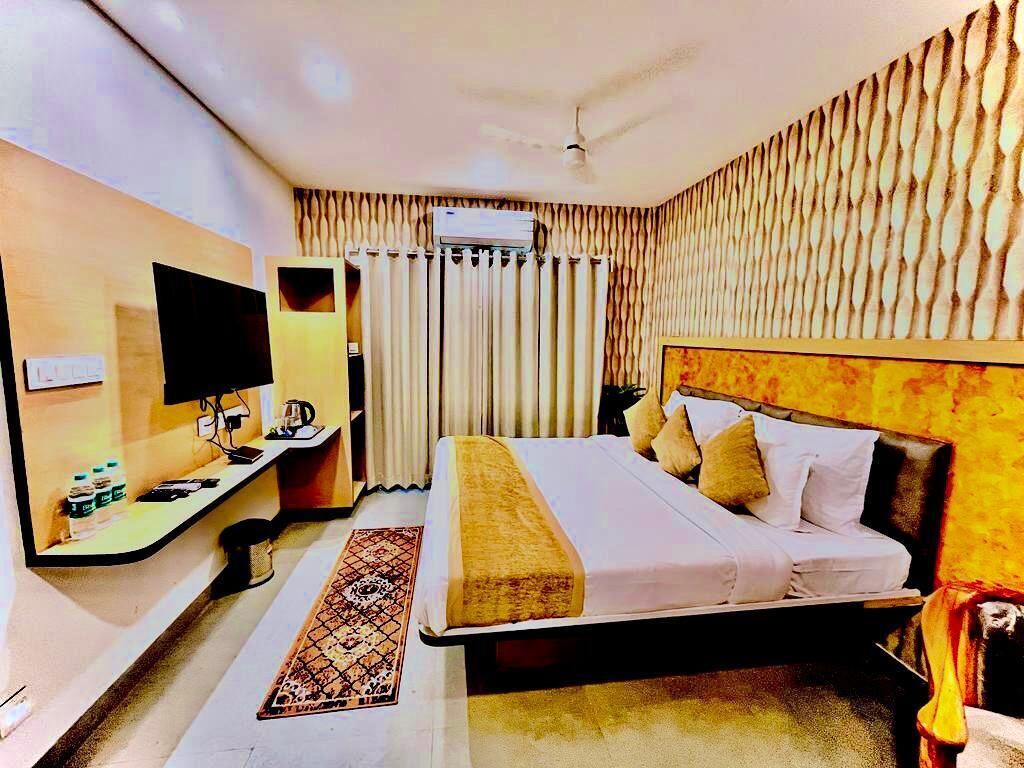 A hotel room with a bed, a desk with a computer, a TV, and a window with curtains.