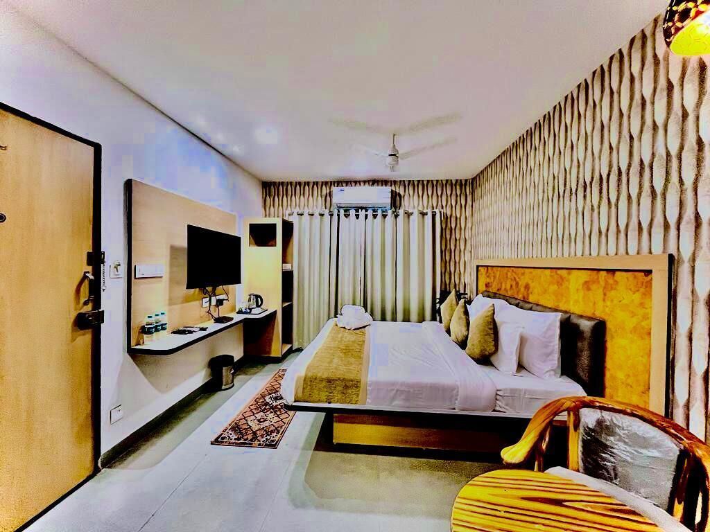 A hotel room with a bed, a desk with a computer, a chair, and a television.