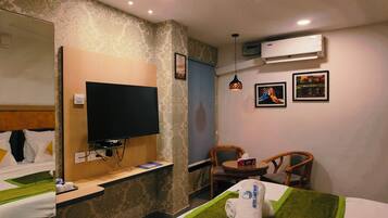 A hotel room with a bed, a television, a desk, a chair, and an air conditioning unit.