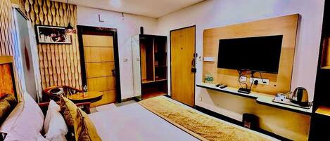 A hotel room with a large bed, a flat-screen TV mounted on the wall, a desk with a chair, and a wardrobe.