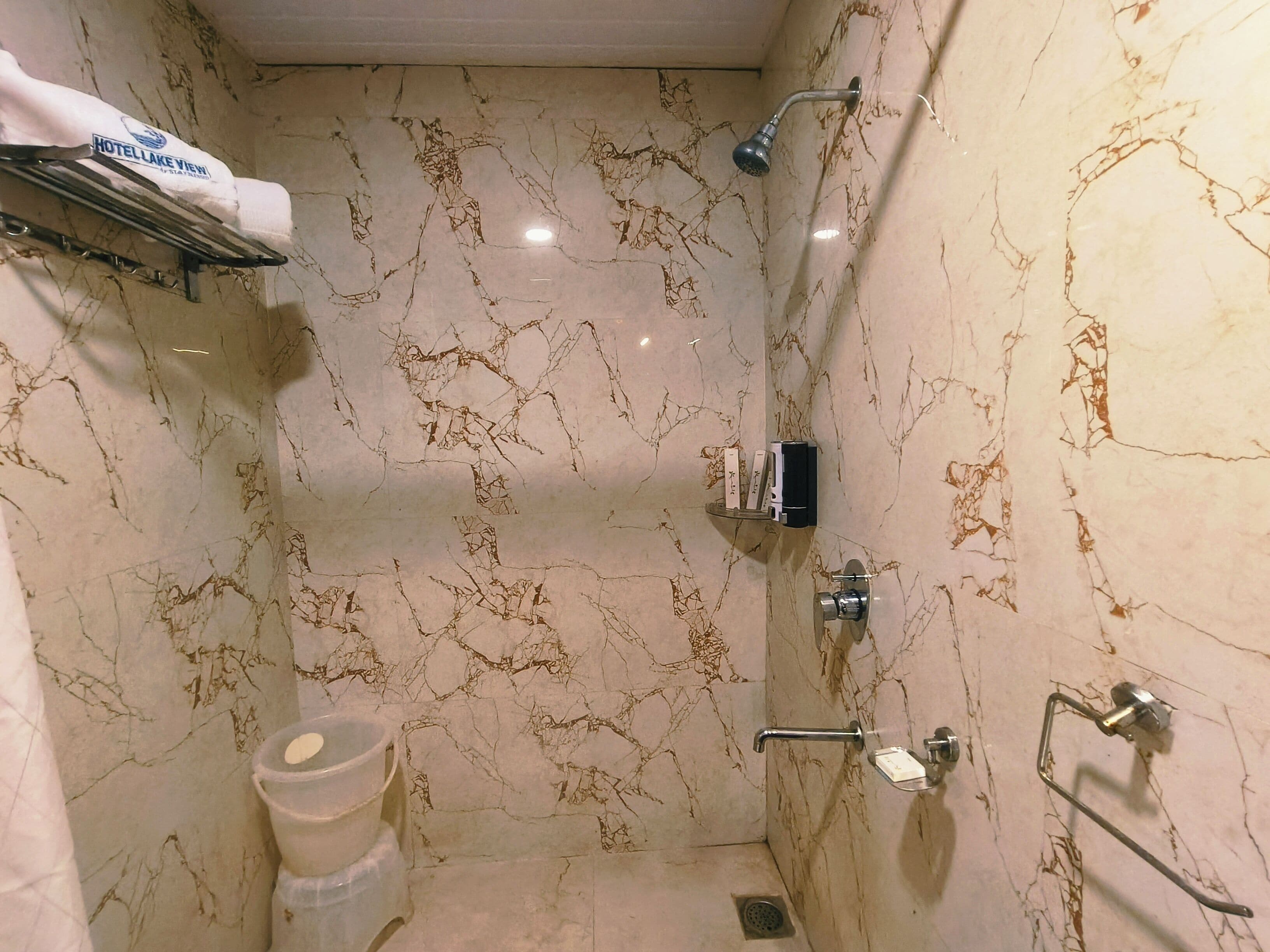 A bathroom with a marble wall, a shower, a toilet, and a towel rack.