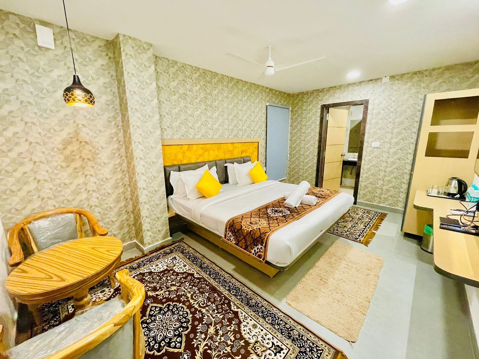 A hotel room with a bed, a wooden chair, a desk, and a mirror.