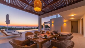 A dining area with wicker chairs and a wooden table set for a meal, overlooking a scenic view.