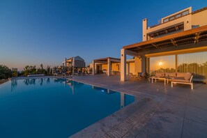 A modern poolside area with a clear pool, lounge chairs, and a building with large windows and a covered patio. - Vita Brevis - Premium Villa 1,5km From The Beach (Rethymno)