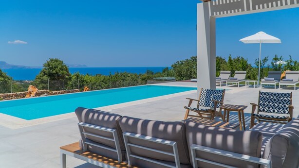 A poolside area with lounge chairs and a pergola overlooking a clear blue pool and the sea.