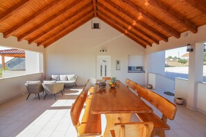 A spacious dining area with a wooden table and benches, a small kitchen area, and a view of the outside. - Villa Zrilić ZadarVillas (Perušić Benkovački)