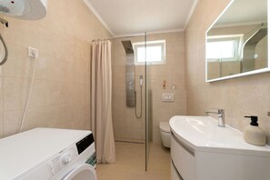 A modern bathroom with a glass-enclosed shower, a standalone washing machine, and a sink with a soap dispenser. - Villa Zrilić ZadarVillas (Perušić Benkovački)