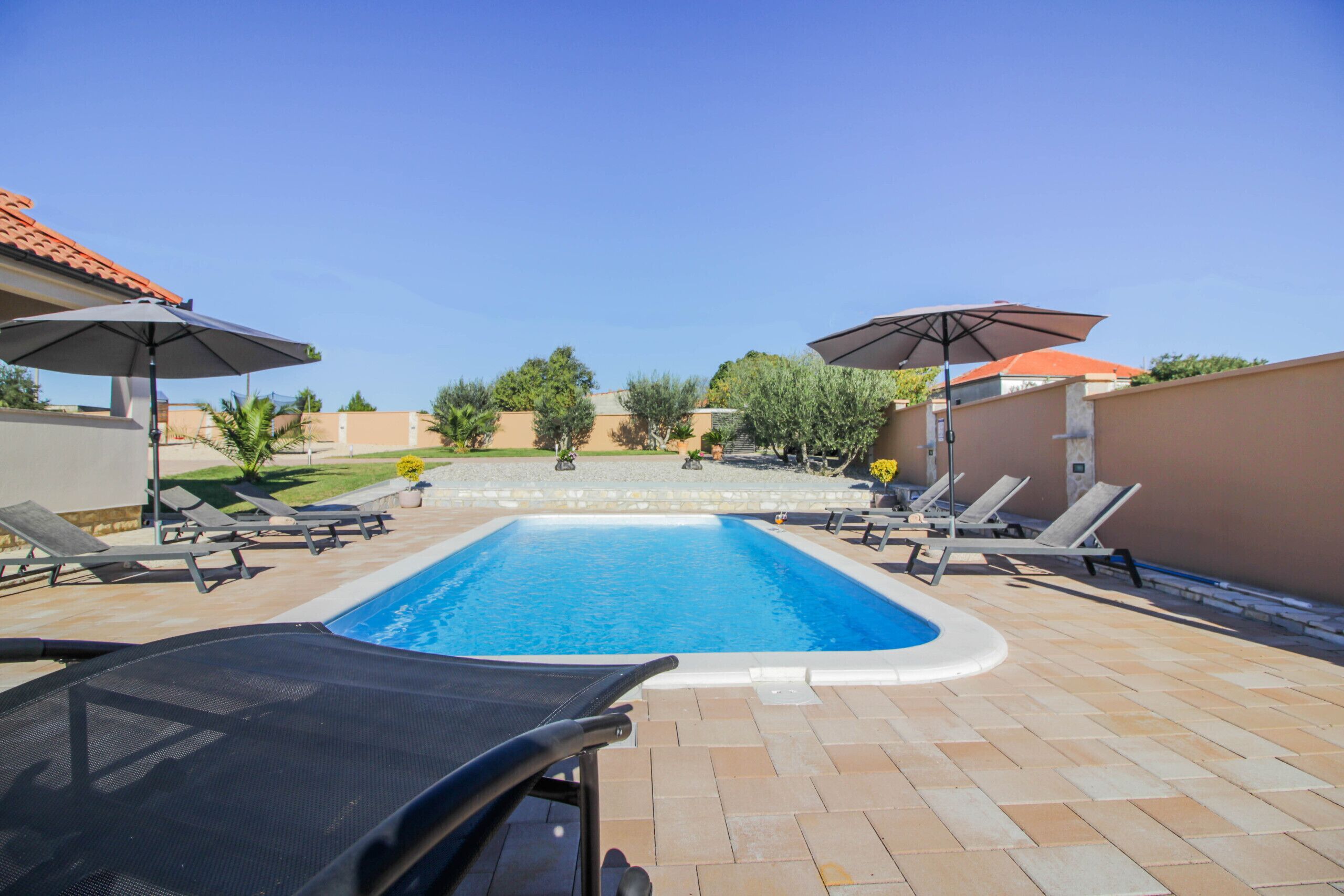 Piscina retangular com deck ladrilhado, rodeada por espreguiçadeiras e guarda-sóis.
