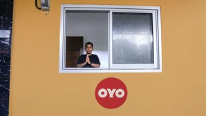 A person standing in a window with a white frame, a wall-mounted intercom, and a large red OYO logo below the window. - OYO 92626 Good Sleep 4 Inn Dcos Syariah (Samarinda)