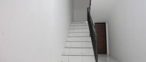A staircase with white tiles and a metal railing, leading to a wooden door.