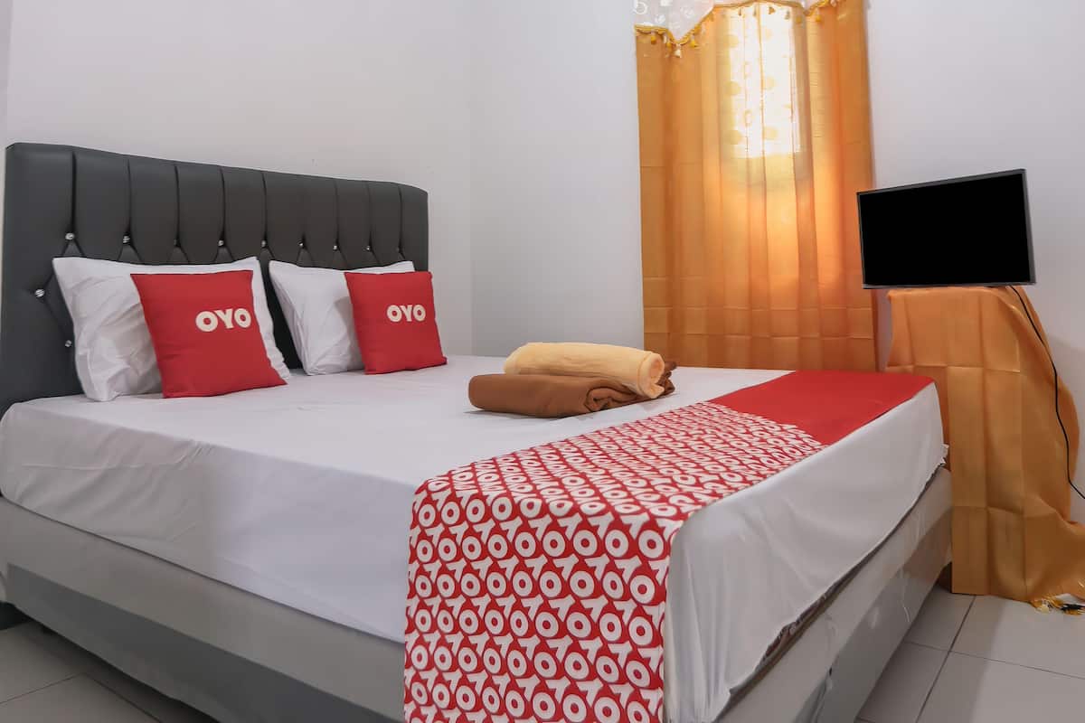 A neatly made bed with a white and red patterned bedspread, two red pillows with the word "OYO" on them, and a brown towel.