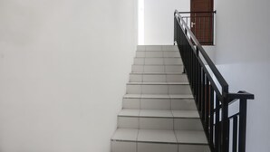 A staircase with white tiles and black railings leading to a wooden door. - OYO 92626 Good Sleep 4 Inn Dcos Syariah (Samarinda)
