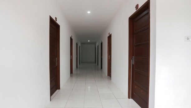 A corridor with white tiled floors and wooden doors on both sides. - OYO 92626 Good Sleep 4 Inn Dcos Syariah (Samarinda)