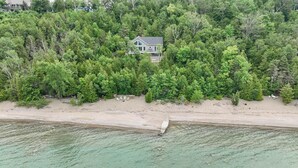 Een huis omringd door dicht bos, met een zandstrand in de voorgrond.