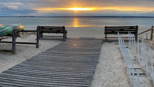 Une promenade en bois menant à une plage où se trouvent des bancs et un kayak.