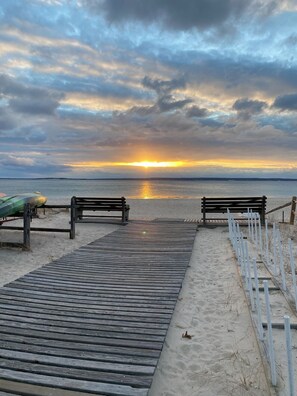 A wooden boardwalk leading to a beach with benches and a kayak.