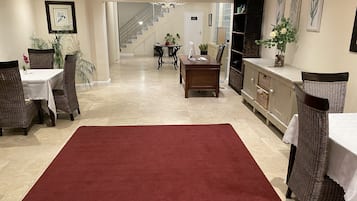 Eine geräumige Hotelhalle mit rotem Teppich, Korbmöbeln, einer Treppe und gerahmten Kunstwerken an den Wänden.