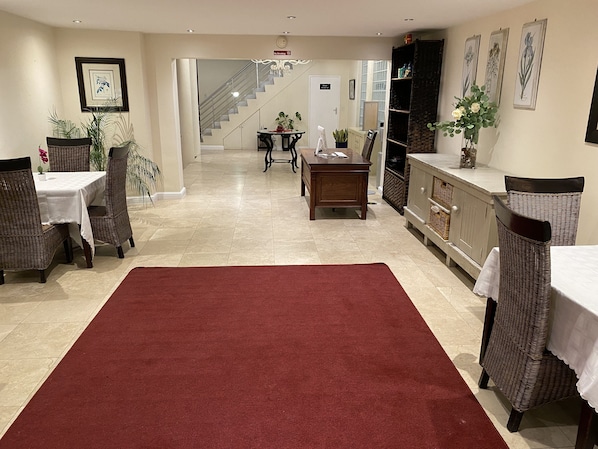 A spacious hotel lobby with a red carpet, wicker furniture, a staircase, and framed artwork on the walls.