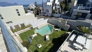 Ein Poolbereich auf dem Dach mit freiem Blick auf den Ozean, umgeben von modernen Gebäuden und ausgestattet mit Liegestühlen sowie einem kleinen Pool.