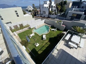 Un espace piscine aménagé sur le toit, offrant une vue dégagée sur l’océan, entouré de bâtiments modernes et doté de chaises longues et d’une petite piscine.