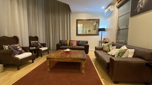 Ein Wohnzimmer mit einem braunen Sofa, zwei Sesseln, einem Holztisch und einem roten Teppich.