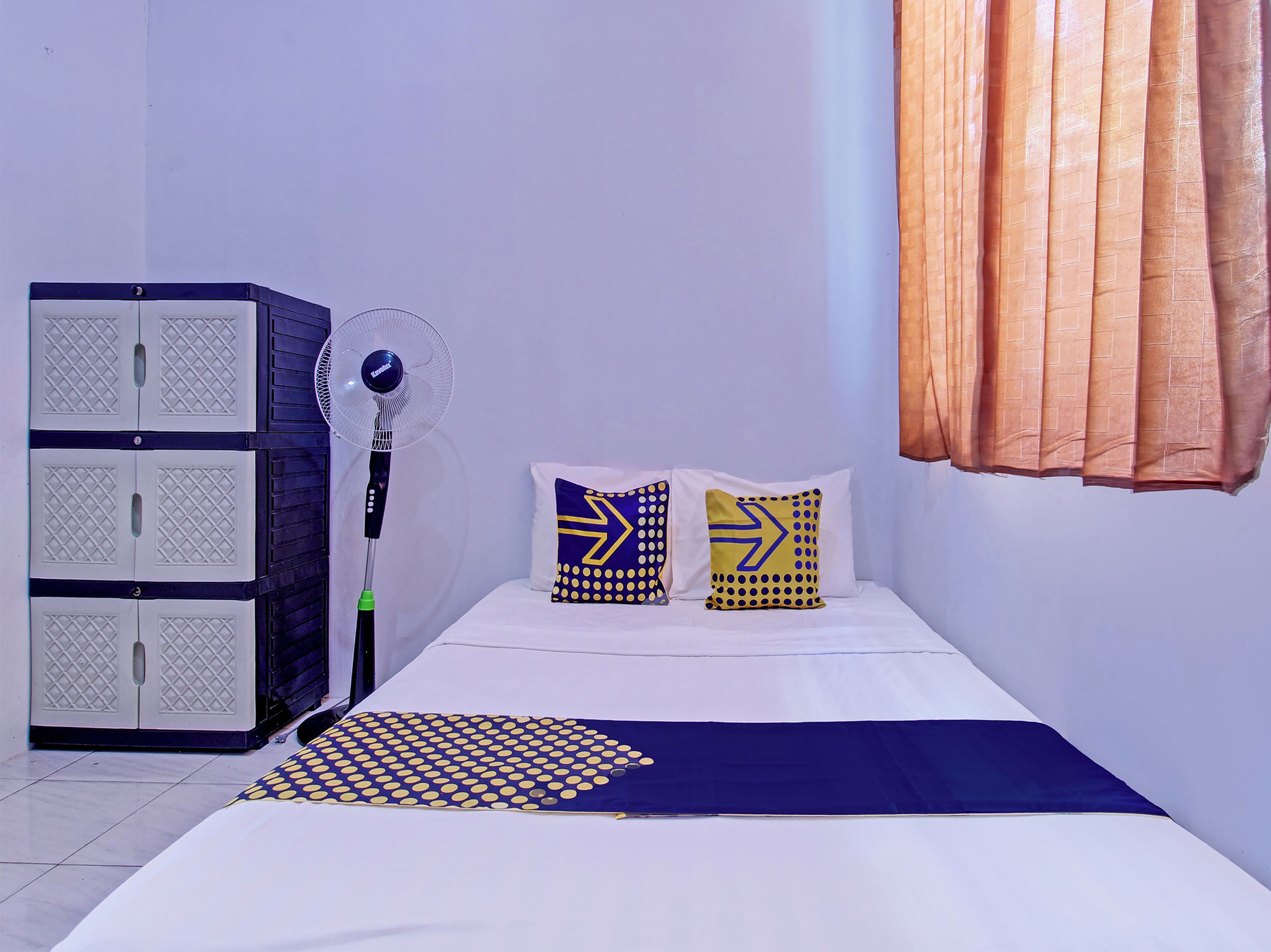 A room with a bed, two pillows, a blanket, a standing fan, and a wardrobe.