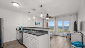 A modern kitchen with white cabinets, a granite countertop, and a built-in island. There is a ceiling fan, pendant lights, and a large window offering a view of the ocean. - New Heated Pool & Hot tub! Fantastic Ocean Views! (Galveston)