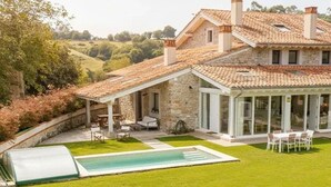 A stone house with a swimming pool, outdoor seating, and a view of the countryside. - Casa con Jardín y Piscina Climatizada Cerca de Comillas a 10 min de la Playa (valdaliga)