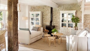 A cozy living room with a stone wall, a fireplace, and white furniture. - Casa con Jardín y Piscina Climatizada Cerca de Comillas a 10 min de la Playa (valdaliga)