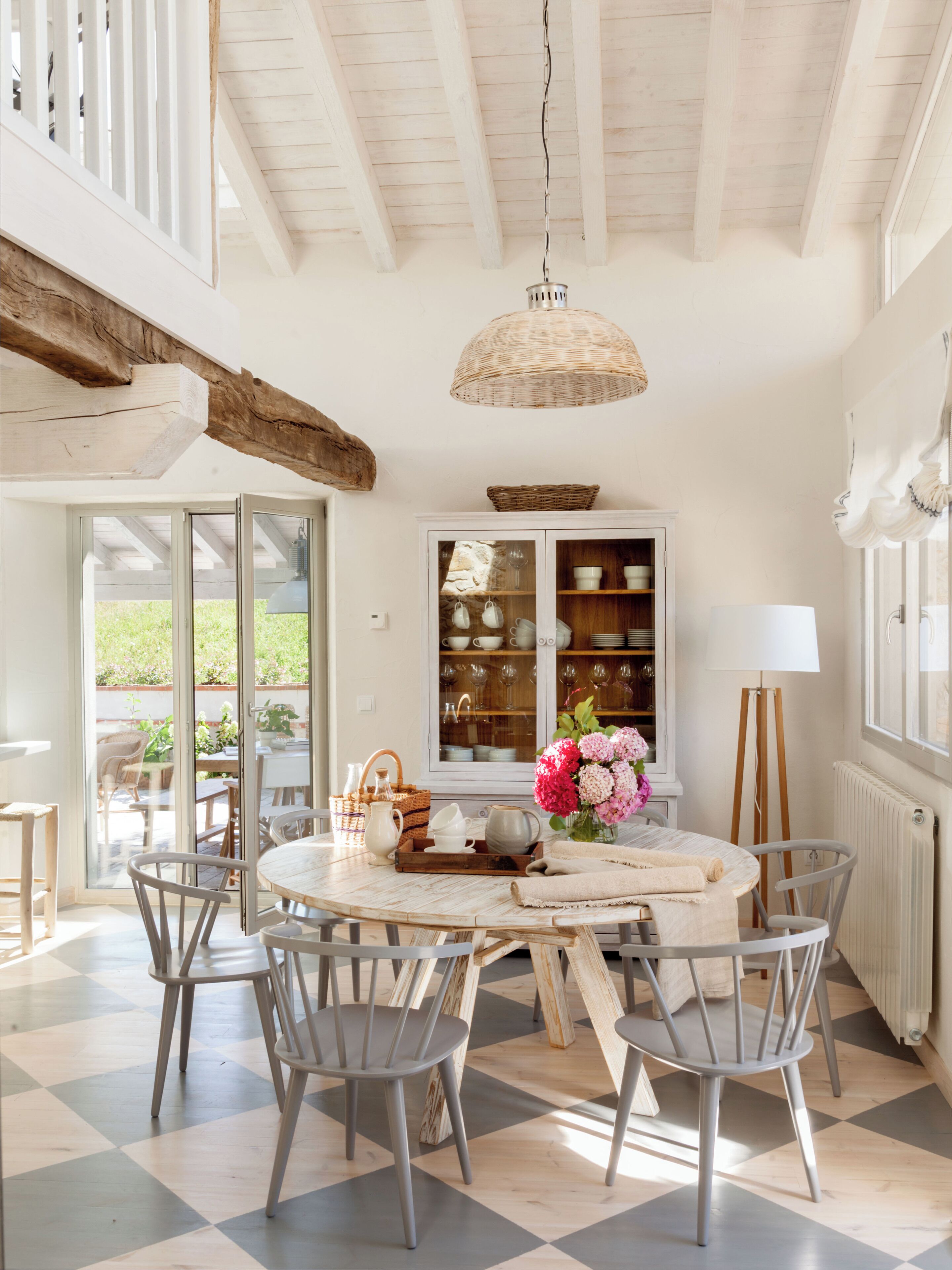 A dining area with a round table, chairs, a hanging light fixture, and a cabinet with glass doors.
