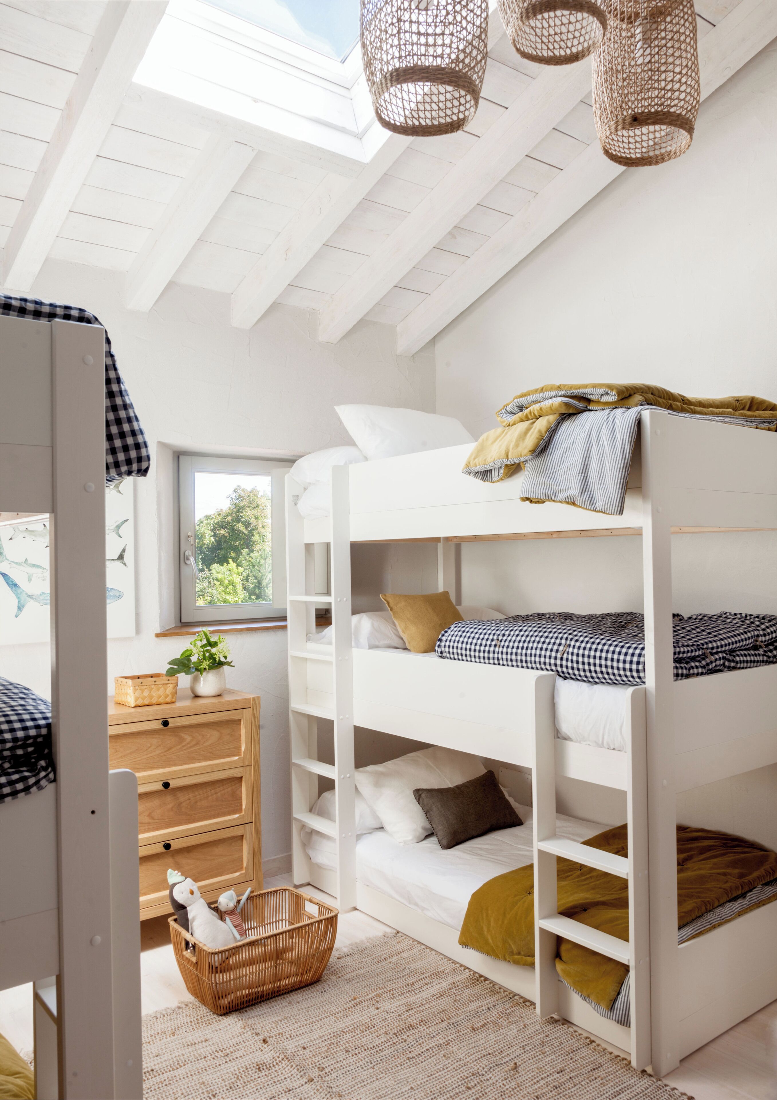 Une chambre avec un lit superposé, une lucarne, une commode en bois et un panier en osier.