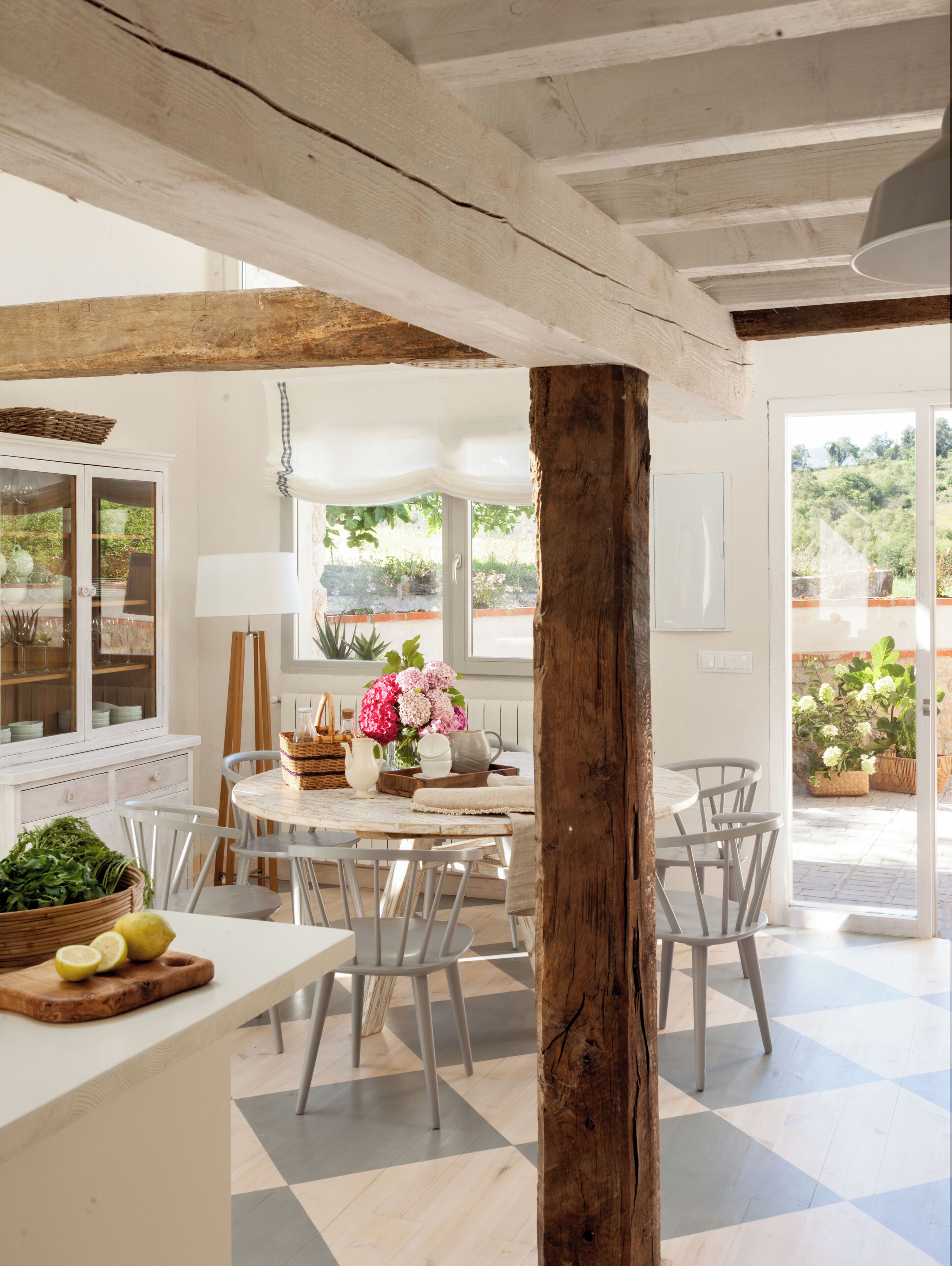 A modern kitchen with a central island, white cabinetry, and a view of the garden through the windows.