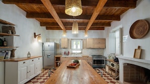 A kitchen with a wooden table, a refrigerator, a stove, and a hanging light fixture. - Villa Canto Antico -SARDINIA UNLIMITED (Porto San Paolo)