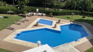Ein großer rechteckiger Pool mit einem kleineren angrenzenden Pool, umgeben von einer gefliesten Liegefläche und Liegestühlen.