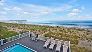 Un espace piscine avec des chaises longues et une vue sur la plage et l’océan.